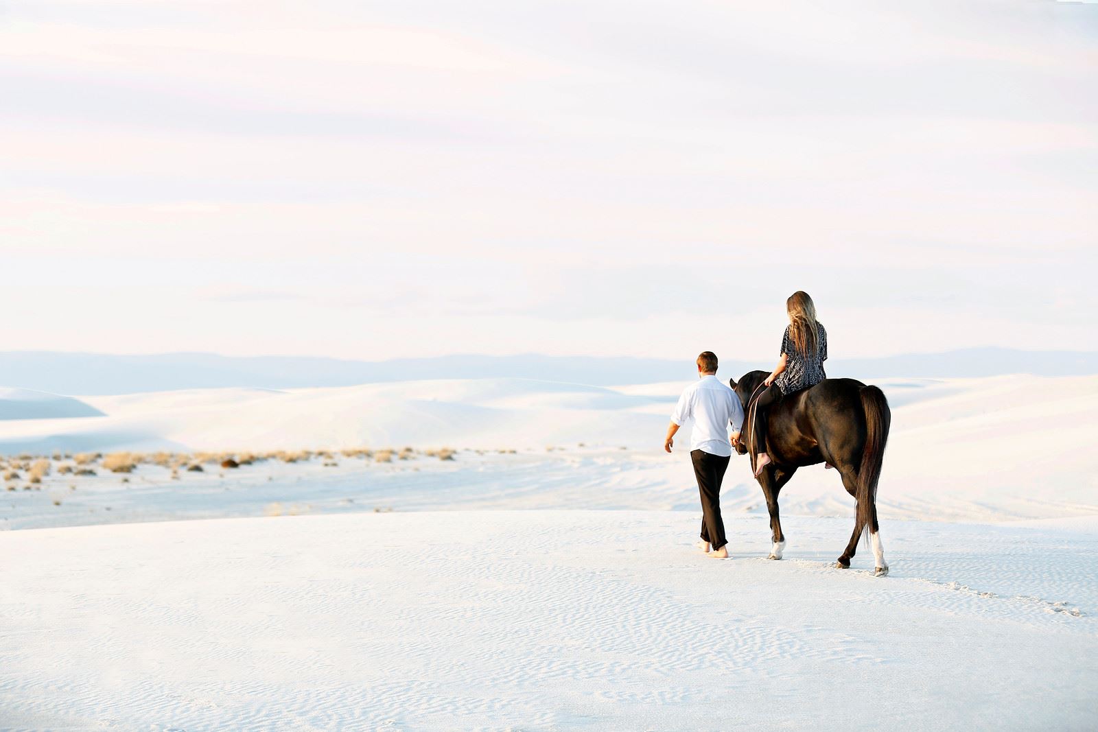 A woman on horseback with a man walking at White Sands National Park.